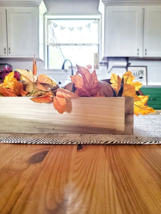 a wooden box centerpiece with faux pumpkins and fall leaves is a perfect match for a rustic table setting
