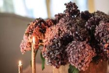 a wooden bucket with purple and rust-colored faux blooms plus elegant gold candles are a stylish combo for the fall