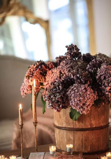 A wooden bucket with purple and rust colored faux blooms plus elegant gold candles are a stylish combo for the fall