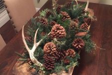 a woodland fall centerpiece of a dough bowl with evergreens, pinecones of various kinds and antlers for autumn