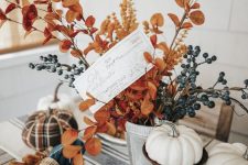 an all-natural fall centerpiece of a planter with berries, bright leaves on branches and faux pumpkins on stands