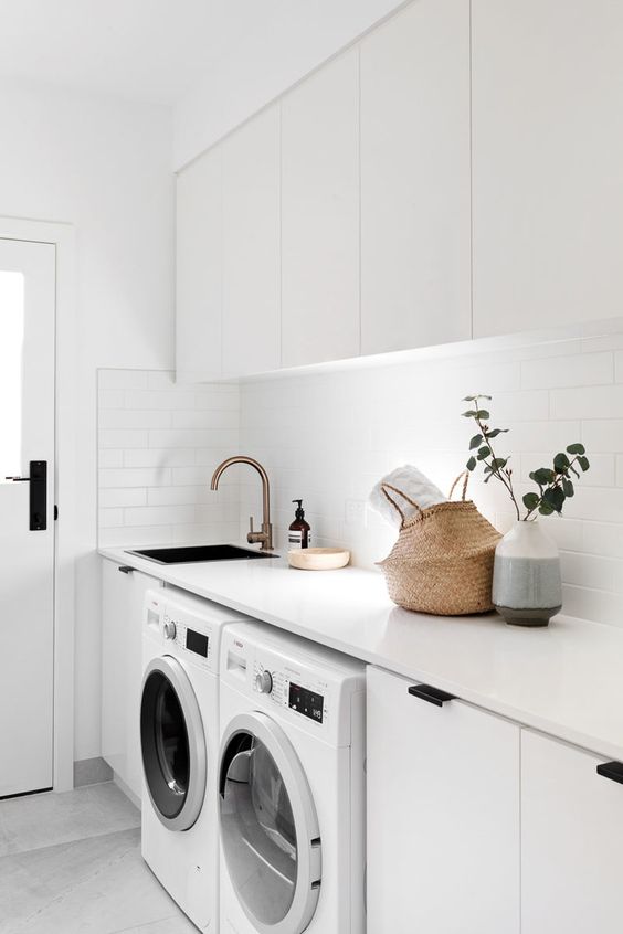 An edgy white laundry with sleek cabinets, black handles, a basket for storage, white appliances and built in lights