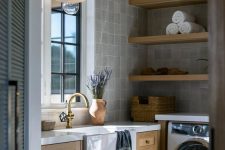 an elegant and welcoming laundry room with grey tiles, open shelves, stained cabinets, stone countertops, pendant lamps and a washing machine and a dryer