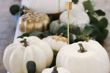 an elegant fall centerpiece of white and gold pumpkins, greenery and elegant candles in gold candleholders