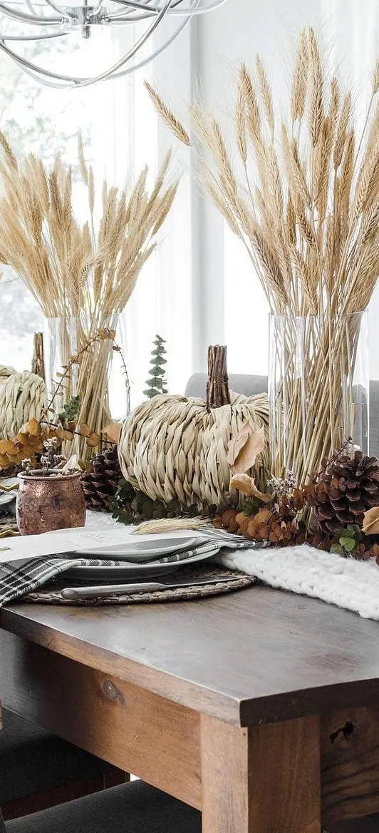 fall table decor with pinecones, leaves, dried foliage, pumpkins made of grass and wheat in glass vases