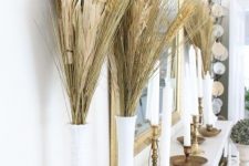 tall white vases with wheat and corn husks and tall and thin candles in candle holders for decorating the mantel