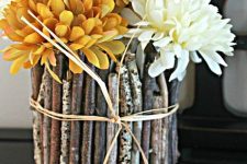 vases covered with twigs and sticks for a woodland feel and bright orange and white blooms for a fall arrangement