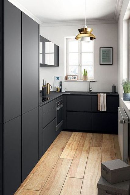 A Scandinavian kitchen with white walls, matte black cabinets and built in appliances, a gold pendant lamp and accessories