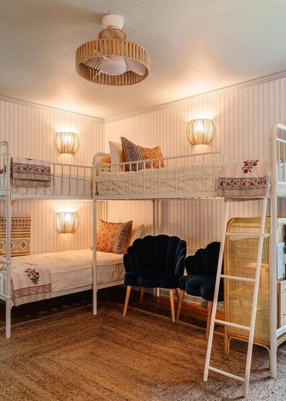 a beach-themed girls' room with white metal bunk beds, printed bedding, a woven rug and a ladder, navy chairs