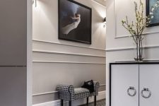 a beautiful entryway with molding on the walls, printed floor and a mini bench, a storage unit with ring pulls and a bold artwork