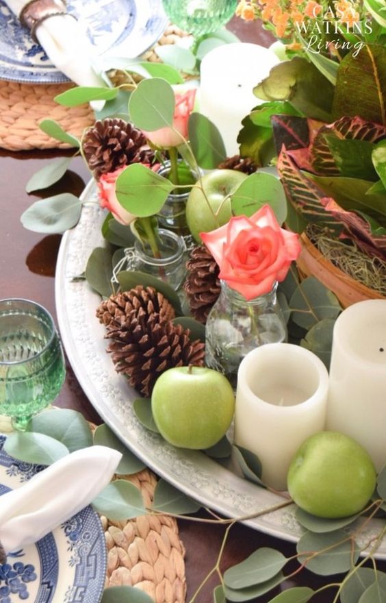 a beautiful fall centerpiece of a silver tray, green apples, pinecones, oliage and coral blooms