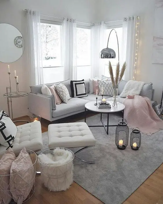 a beautiful living room with a grey sectional, pink, white and grey and pink blankets, a creamy chair and pink pillows