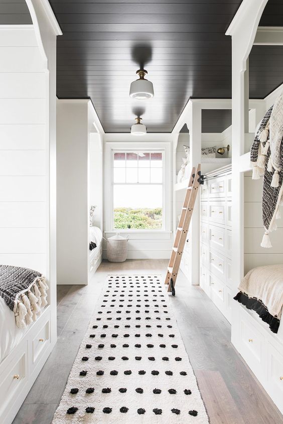 A black and white kids' bedroom with built in usual and bunk beds, with a built in oversized dresser and a ladder