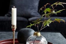 a black coffee table, a red tray, a glass candle holder, a clear vase with foliage and soem candles for an elegant feel