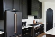 a black farmhouse kitchen with shaker cabinets, a shiplamp hood, white countertops, gold handles and a black and white kitchen island