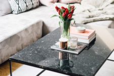 a black marble coffee table with some books, candles in candle holders and an arrangement of red tulips in a vase