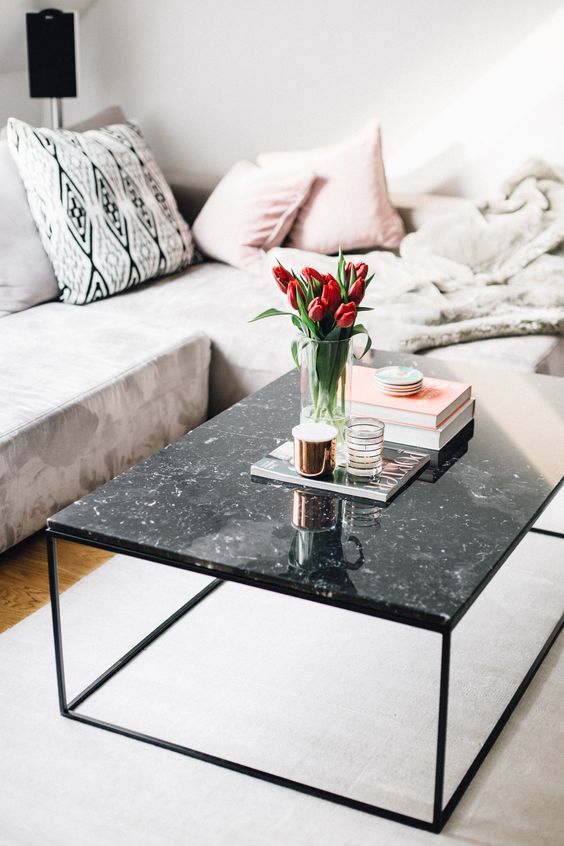 a black marble coffee table with some books, candles in candle holders and an arrangement of red tulips in a vase