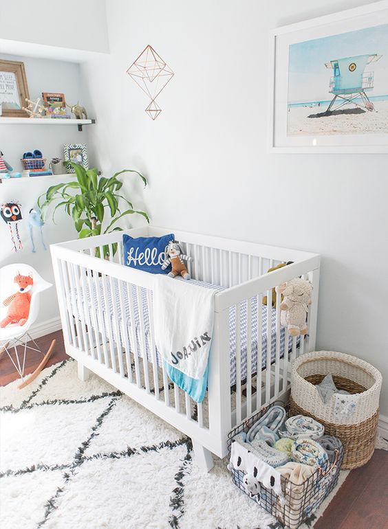 A bright beach inspired nursery with a white Sundvik crib, baskets, open shelving, a beach artwork and some printed textiles