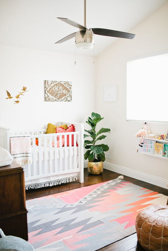 a bright boho nursery with a colorful rug, books, a leather ottoman and artworks plus an IKEA Sundvik crib