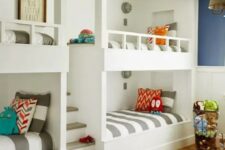 a bright kids’ room with navy and white walls, white built-in bunk beds, striped bedding and a printed rug is a cool space
