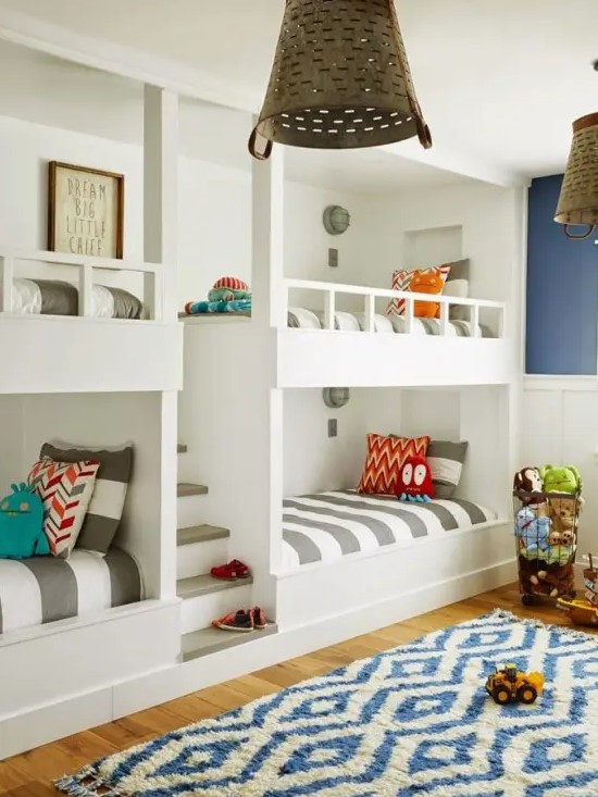 A bright kids' room with navy and white walls, white built in bunk beds, striped bedding and a printed rug is a cool space
