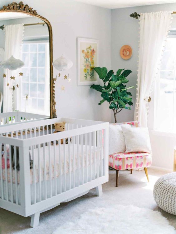 a bright nursery with an IKEA Sundvik crib, a statement mirror in a vintage frame, a bright chair, potted plants and a knit ottoman