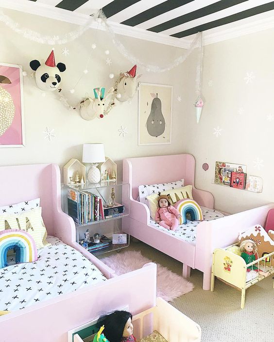 a bright shared girls' bedroom with pink IKEA Sundvik beds, faux animal heads, bright toys and banners