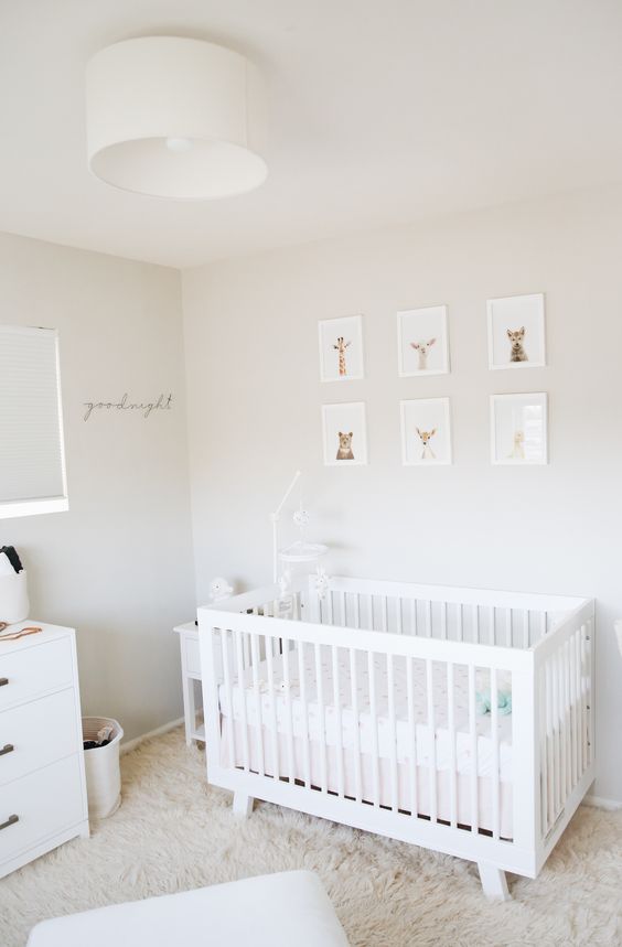 A calming neutral nursery with a gallery wall of animal portraits, a white IKEA Sundvik crib, a faux fur rug and some whites and off whites
