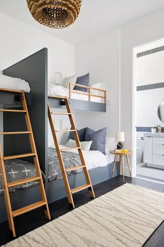 A catchy and contrasting graphite grey and white kids' room with four built in bunk beds, wooden ladders and a side table, a wooden pendant lamp