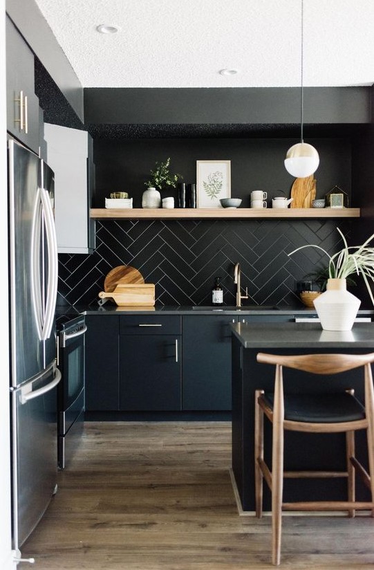 A chic black kitchen with black cabinets, a tile backsplash, concrete countertops and touches of light colored wood