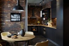 a chic black kitchen with matte cabinets, a brick backsplash, butcherblock countertops and a dining space