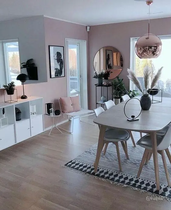 a chic dining space with pink walls, a stained table, grey chairs, a copper lamp and pink pillows
