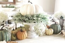 a chic fall centerpiece of a white pumpkin with lots of greenery on a white stand and faux pumpkins on the table