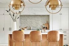 a chic glam kitchen with white cabinetry, peachy stools with gold legs, a peachy kitchen island and copper pendant lamps