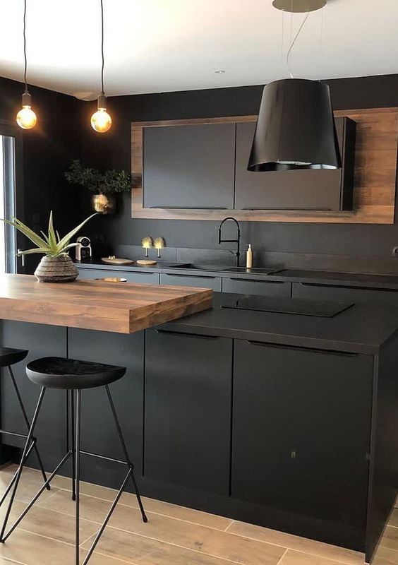 A chic matte black kitchen with metal cabinets and a kitchen island, a rich stained countertop, a black pendant lamp and stools