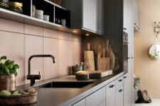 a chic modern kitchen with grey cabinetry and black countertops, a matte pink tile backsplash and black fixtures