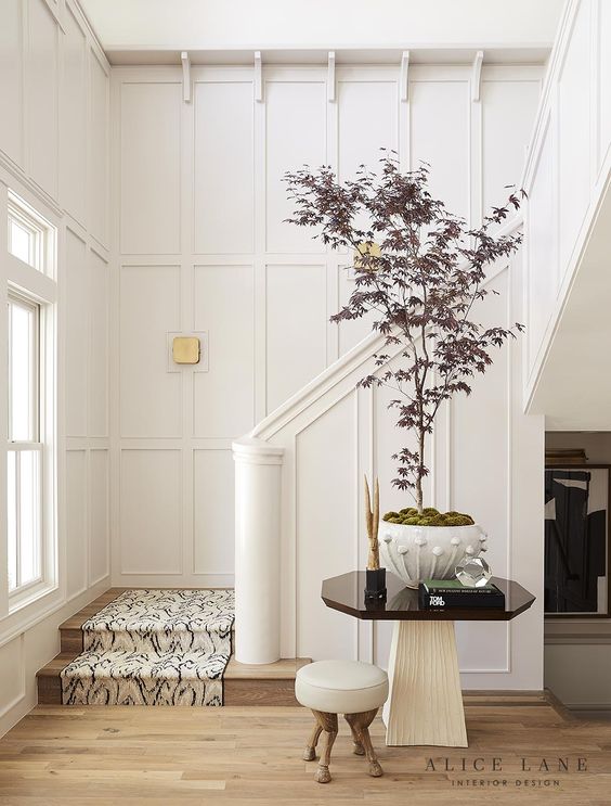 A chic neutral entryway with molding, with light stained floor, a large and catchy plant for a statement is amazing
