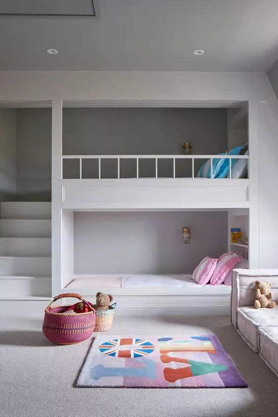 A clean minimal kids' room with built in bunk beds, bright bedding and a rug, a low seat sofa by the window, baskets for storage and built in lights