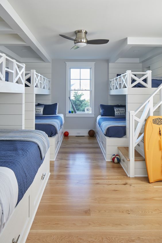 a coastal kids' bedroom with built-in bunk beds, navy and blue bedding, built-in ladders and a surf