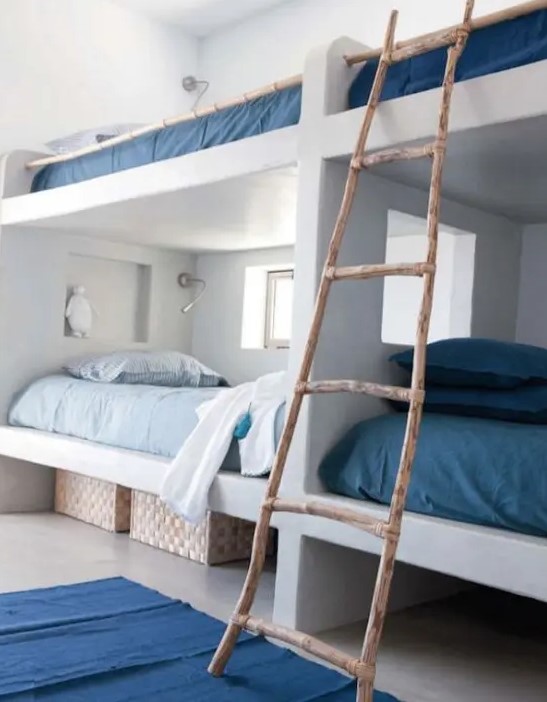 A coastal space with white built in bunk beds, with blue and navy bedding, with a ladder and navy rugs is a stylish space with love to the sea