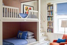 a colorful kids’ room with built-in bunk beds, bright bedding, an orange chair, built-in shelves and a blue rug is a very welcoming space