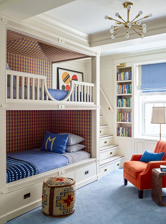 A colorful kids' room with built in bunk beds, bright bedding, an orange chair, built in shelves and a blue rug is a very welcoming space
