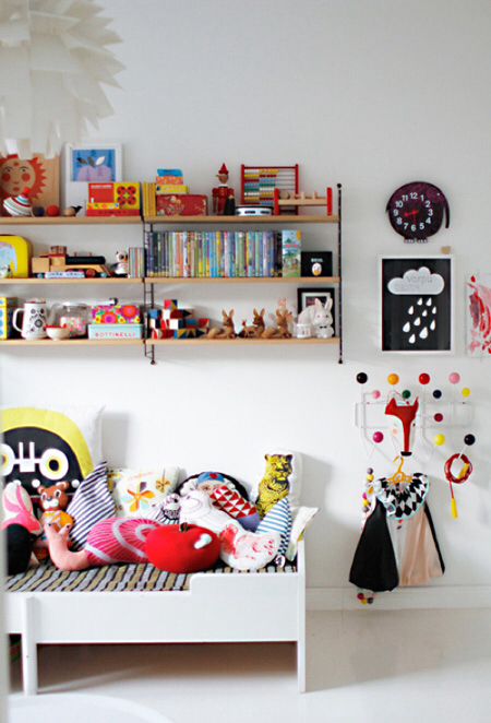 a colorful kid's room with lots of artworks, a large bookshelf, toys, pillows and a white Sundvik bed