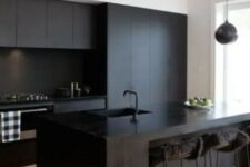 a contemporary black kitchen with sleek cabinets, a wooden kitchen island, stools with faux fur and a pendant lamp