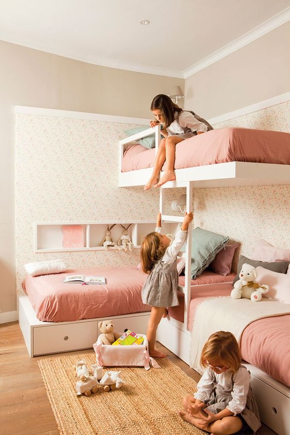 a cozy and pretty girls' bedroom with three bunk beds, pink bedding, printed wallpaper and a woven rug