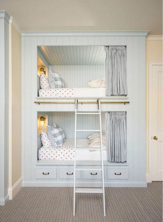 a cozy built-in bunk bed unit in pale blue, with wall lamps, a ladder, curtains and storage drawers in the lower part