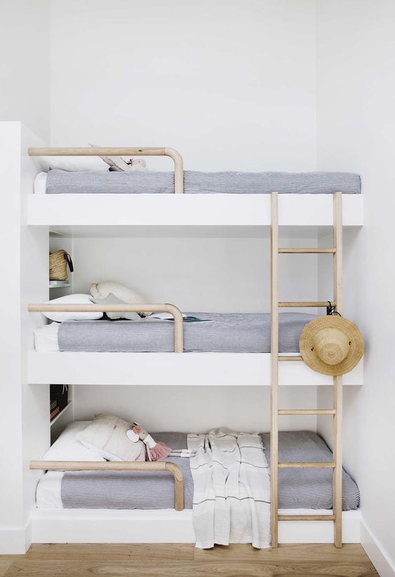 a dreamy coastal sleeping nook with a triple bunk bed, navy and white bedding, wooden ladders and a straw hat looks dreamy
