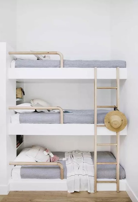 a dreamy coastal sleeping nook with a triple bunk bed, navy and white bedding, wooden ladders and a straw hat looks relaxing