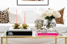 a glam black and gold coffee table with stacks of books, pink candles in floral candle holders, white blooms in a clear vase
