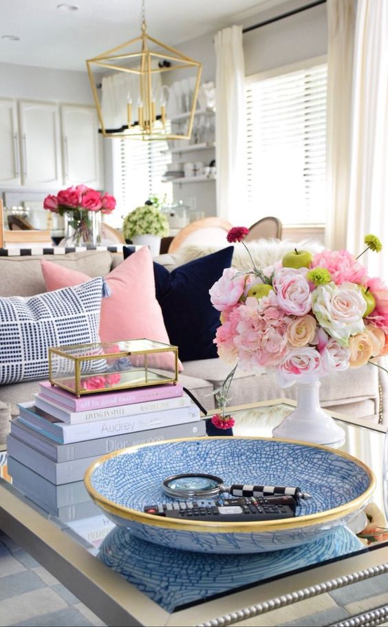 a glam gold and blue coffee table with a blue bowl, a stack of books, bright blooms in a white vase